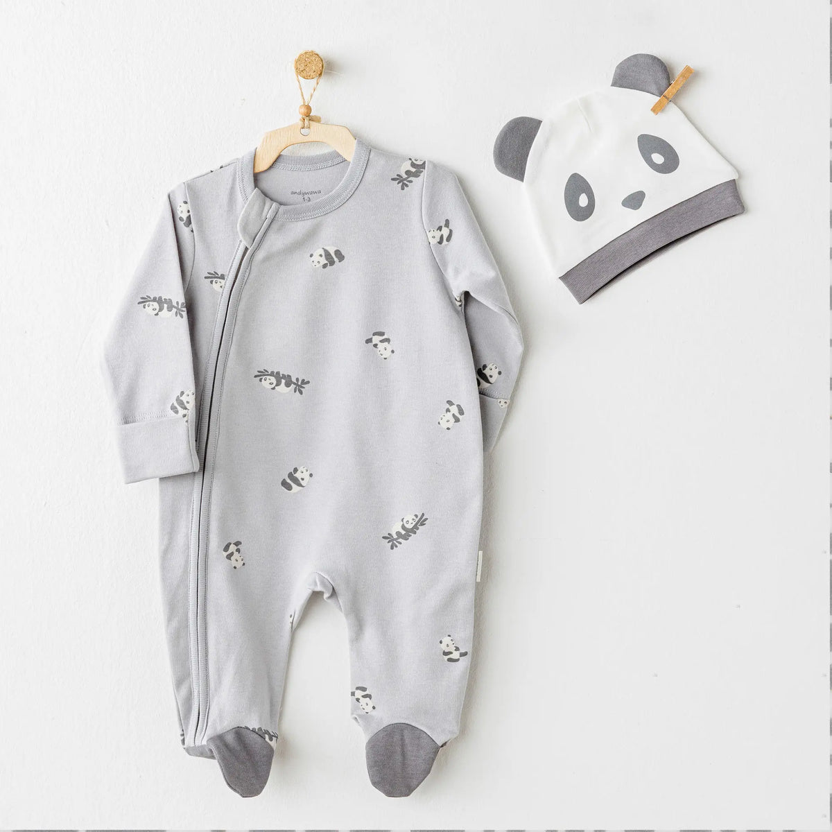 Ensemble pyjama gris pour bébé avec motif panda adorable, zip sur le côté et bonnet assorti tête de panda. Confort 100% coton pour les premières semaines et mois.